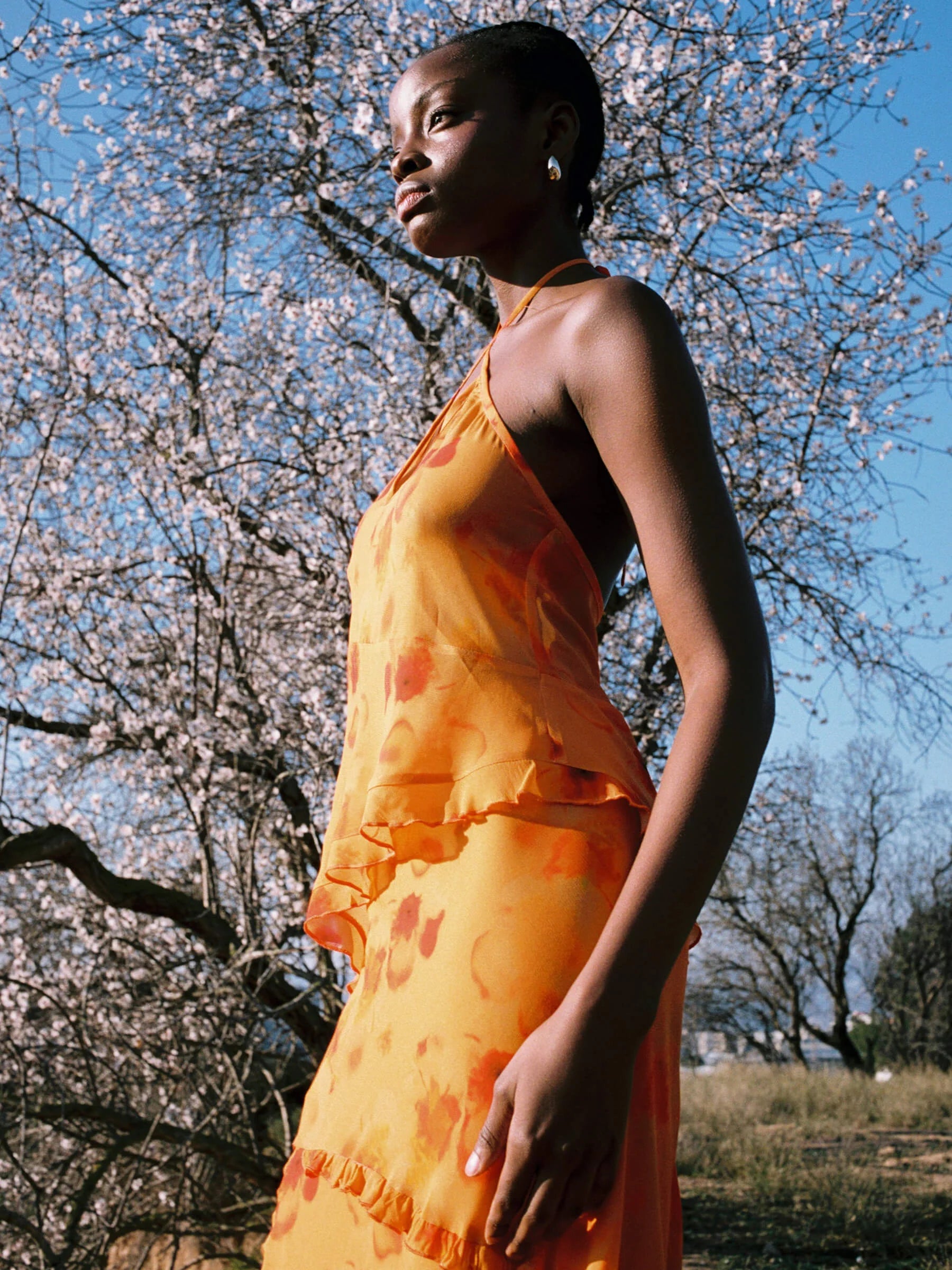 Orange halter neck blouse outdoor side view with slit neckline and asymmetrical ruffled hem lightweight summer blouse