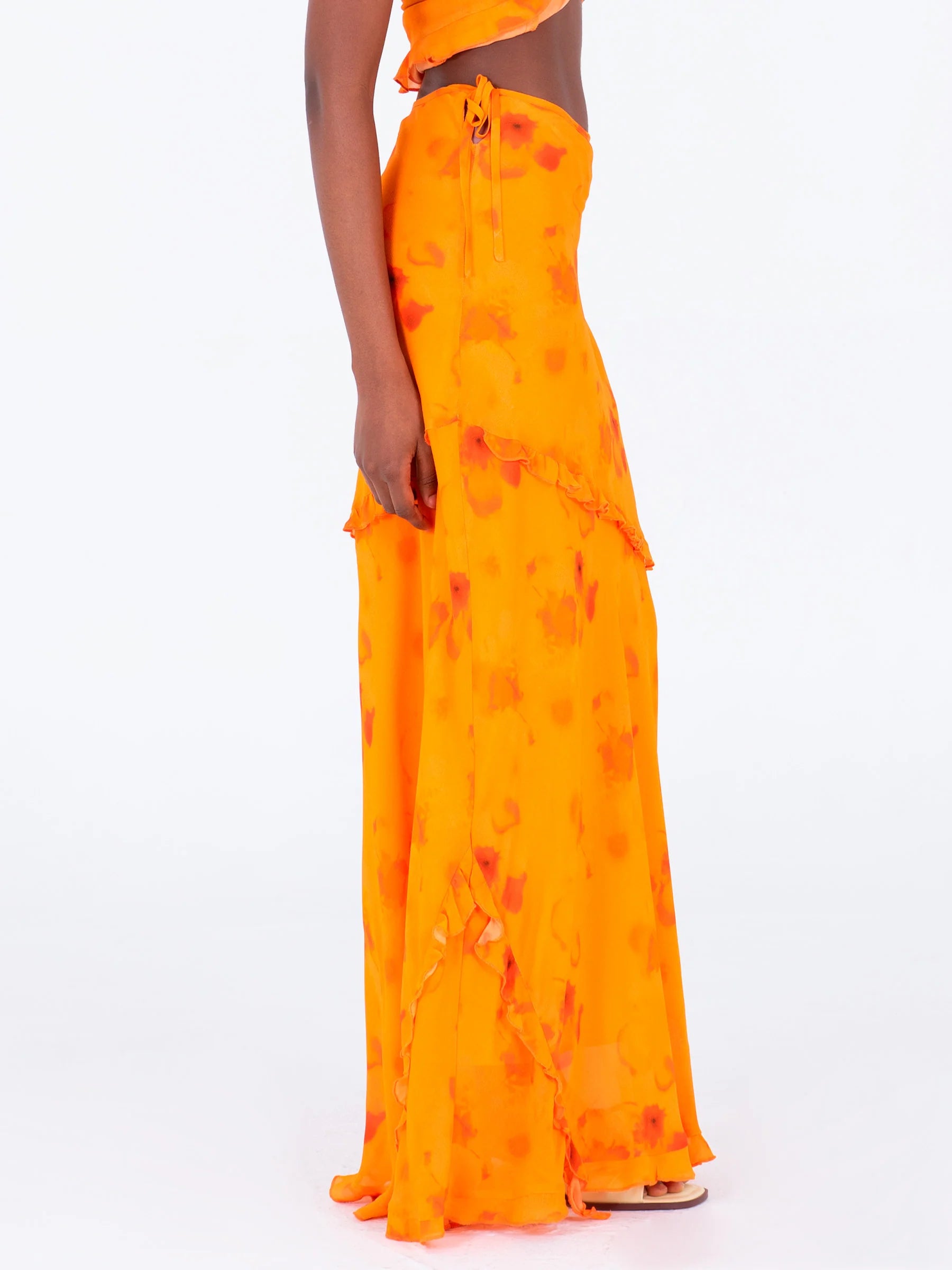 Orange long low rise skirt side view highlighting ruffle detailing and adjustable side straps flowing viscose fabric